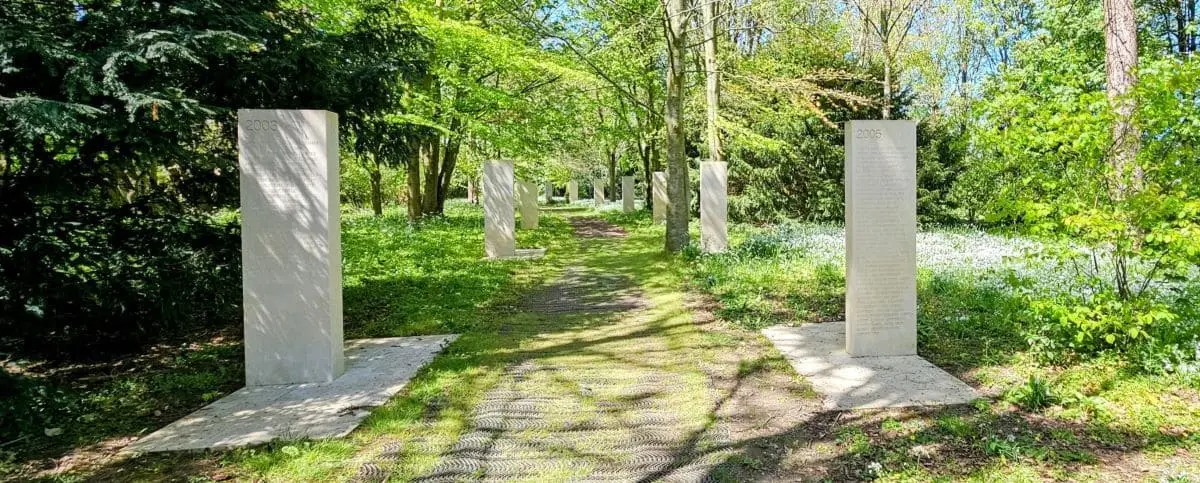 Stone pillars with engraved names set along a green, tree-lined path, part of the memorial honoring fallen journalists.