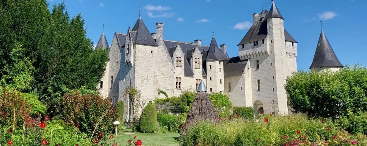 A charming, white stone castle with multiple turrets and a beautiful garden filled with vibrant flowers and lush greenery.