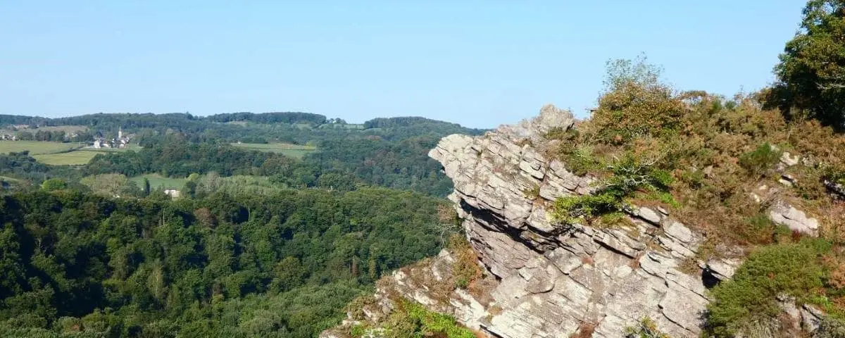 Rocky outcrop overlooking a dense, green forest and rolling hills, offering a stunning panoramic view of the landscape at Roche d'Oëtre.