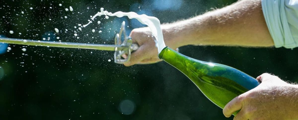 A person performing sabrage, a traditional technique of opening a champagne bottle with a sword, with champagne spraying out.