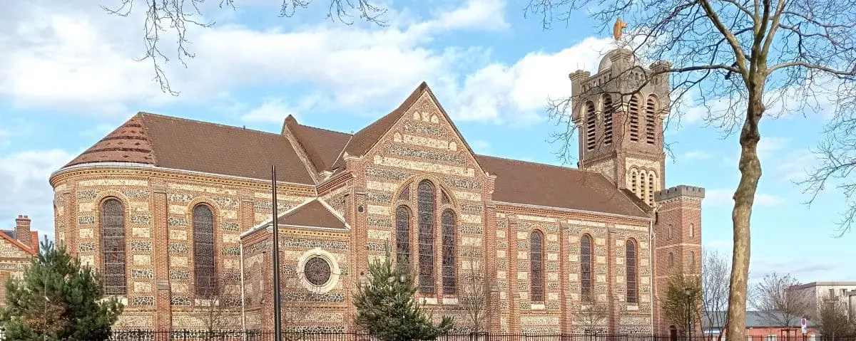The Sacre Coeur Church in Le Havre, featuring intricate brickwork and a tall bell tower topped with a cross, under a blue sky.