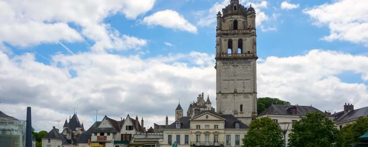 The tall, historic Saint-Antoine Tower in Loches, standing prominently against a backdrop of other historic buildings and a partly cloudy sky.