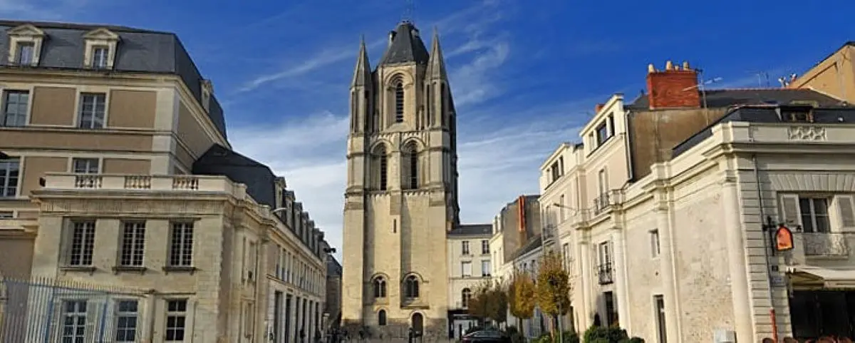Street view of Saint Aubin Church Tower, a tall, historic stone structure surrounded by classic French buildings under a blue sky.