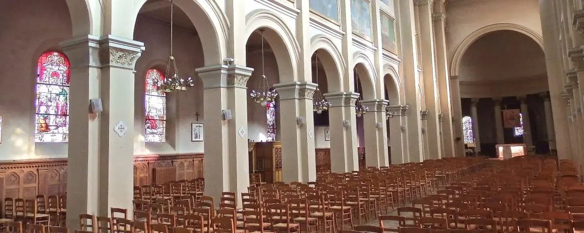 The spacious interior of Saint Augustin Church in Deauville, with rows of wooden chairs and stained-glass windows.