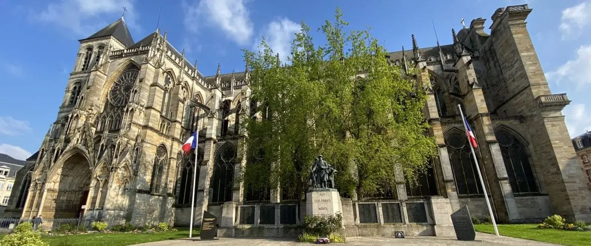 The majestic Saint-Etienne Cathedral with its gothic architecture, large stained glass windows, and intricate stone details. A statue and flags are positioned in front of the cathedral, enhancing its grandeur.