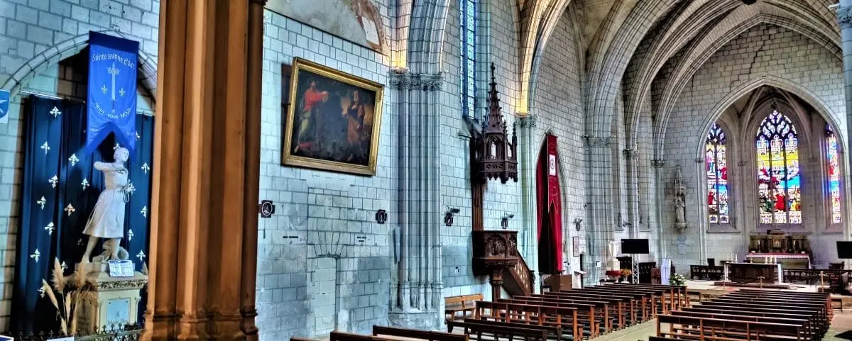 The interior of Saint-Étienne Church in Chinon, featuring gothic architecture, high arched ceilings, stained glass windows, and rows of wooden pews.
