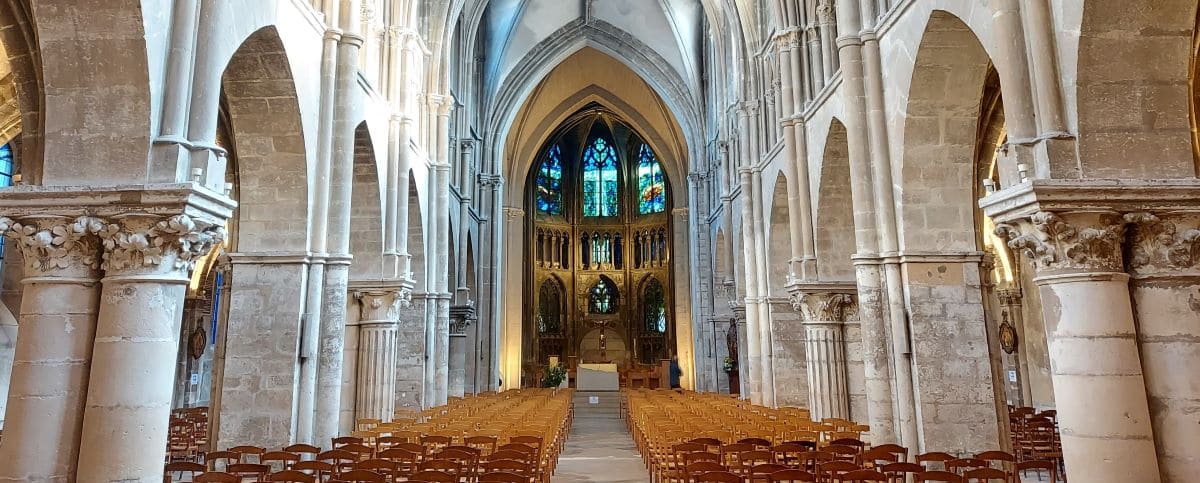 Interior of the Saint Jacques Church in Reims, featuring high arched ceilings, rows of wooden chairs, and colorful stained glass windows.