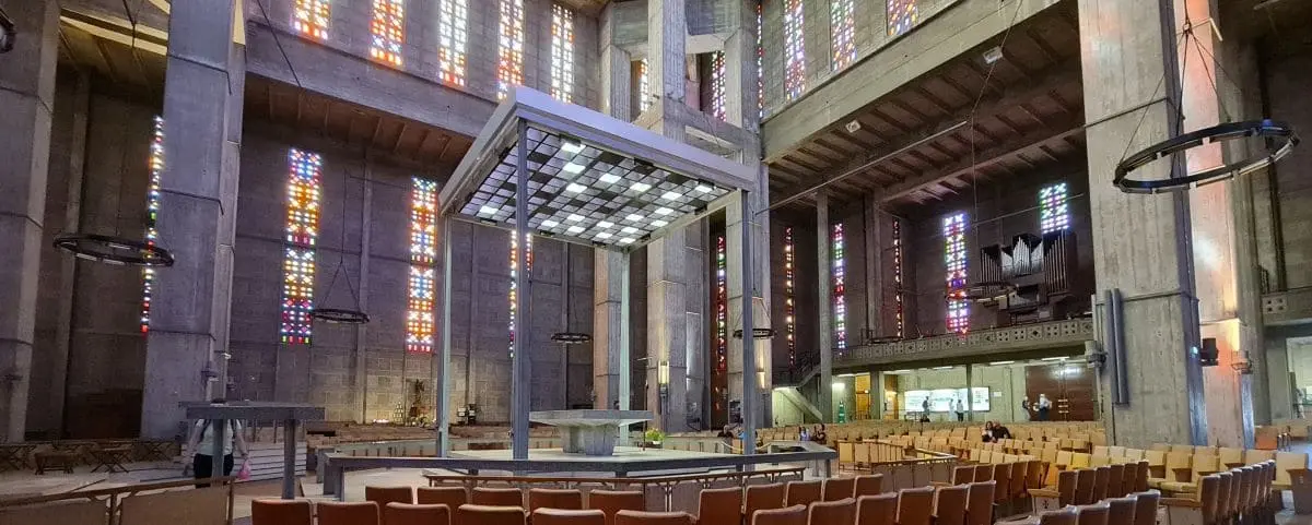 The interior of Saint Joseph Church in Le Havre, showcasing a modern design with tall concrete columns and colorful stained glass windows.