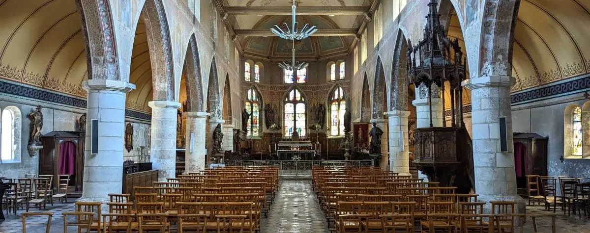 The interior of Saint Leonard Church, characterized by its high arched ceilings, stone columns, and detailed stained glass windows. Wooden chairs are neatly arranged facing the altar.
