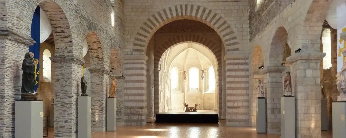 Interior of Saint Martin Church featuring Romanesque architecture with stone arches, sculptures on pedestals, and a bright, arched apse.