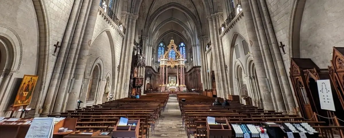 Grand interior of Saint Maurice Cathedral with high vaulted ceilings, ornate altar, and rows of wooden pews.