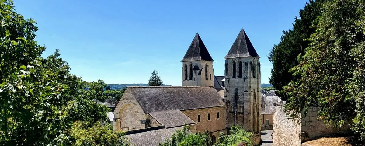 An exterior view of Saint-Mexme Church in Chinon, showcasing its twin steeples and stone façade surrounded by greenery.