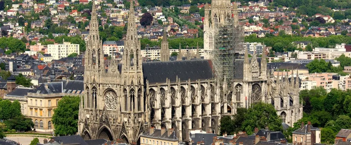 An aerial view of the majestic Saint-Ouen Abbey in Rouen, with its expansive Gothic architecture, towering spires, and the surrounding cityscape.