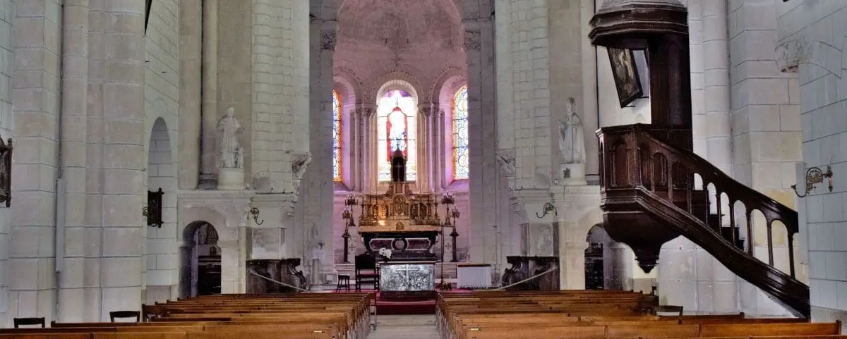 The interior of Saint-Ours Church in Loches, characterized by its vaulted ceilings, stone columns, wooden pews, and a richly decorated altar area.