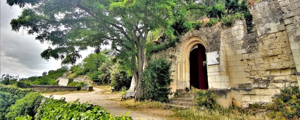 The entrance to Saint-Radegonde Chapel in Chinon, featuring a rustic stone archway surrounded by trees and a path leading to the chapel.