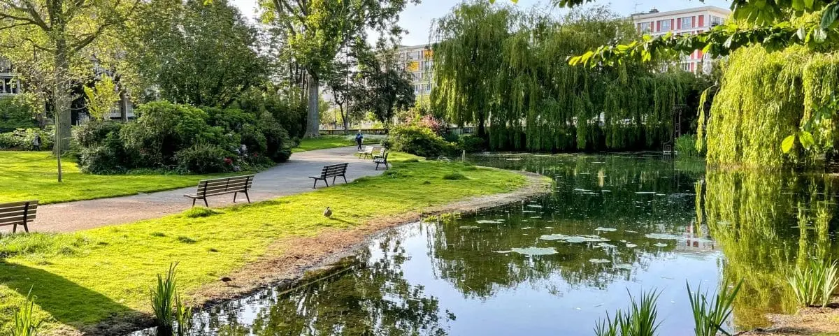 A serene scene at Saint Roch Park in Le Havre, with a pond surrounded by lush greenery, benches, and a walking path.