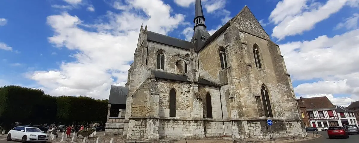 The Saint Sauveur Church with its distinct medieval architecture, featuring a tall spire and stone walls, set against a blue sky with scattered clouds.