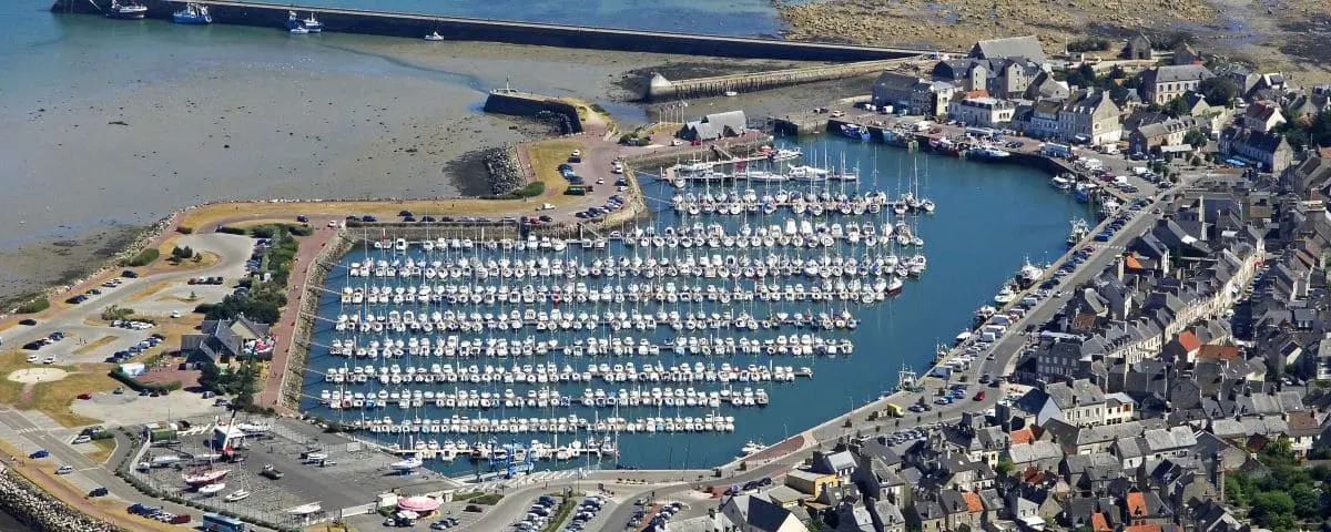 Aerial view of Saint-Vaast-la-Hougue village, focusing on a marina filled with boats and the surrounding quaint buildings.
