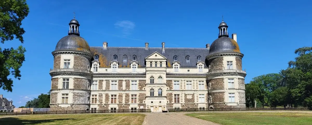 A grand, symmetrical castle with round towers and a central building, featuring detailed stonework and a well-maintained lawn.