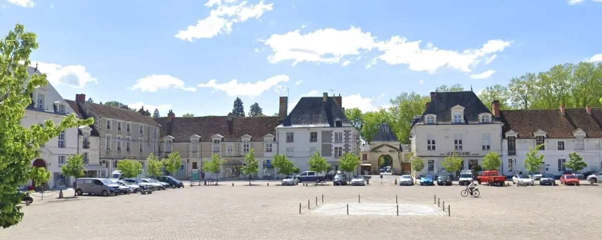 A picturesque square in Richelieu surrounded by historic buildings, with a central area for parking and a few cars scattered around.