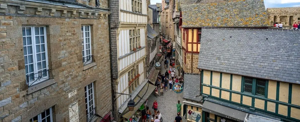 A bustling narrow street in Mont Saint-Michel, lined with historic buildings and crowded with tourists.