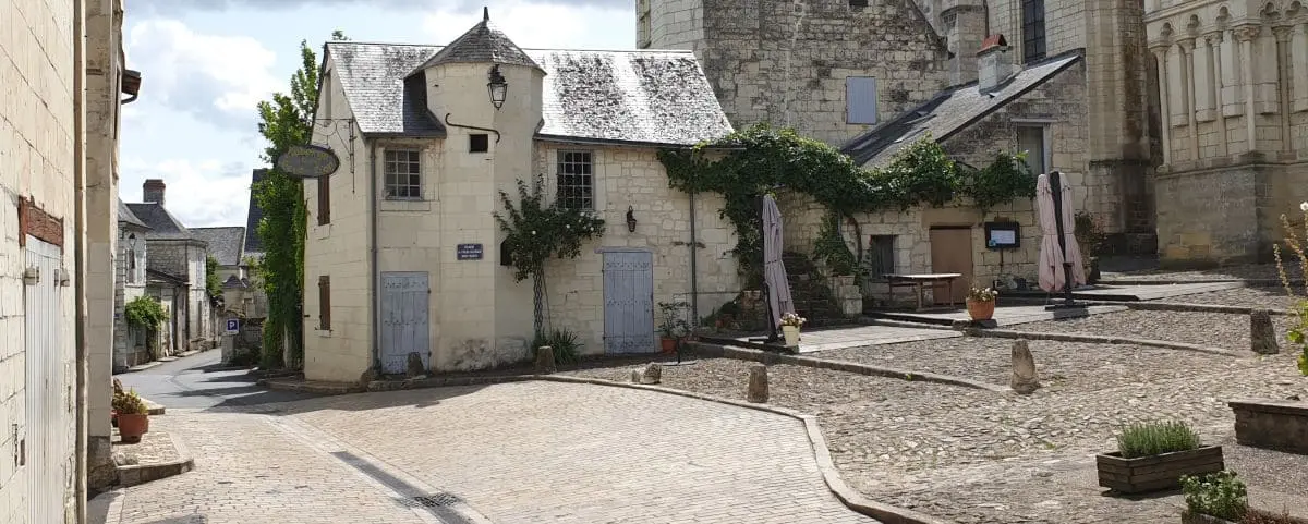 A picturesque cobblestone street in Candes-Saint-Martin, lined with historic stone buildings and greenery, leading to a serene square.