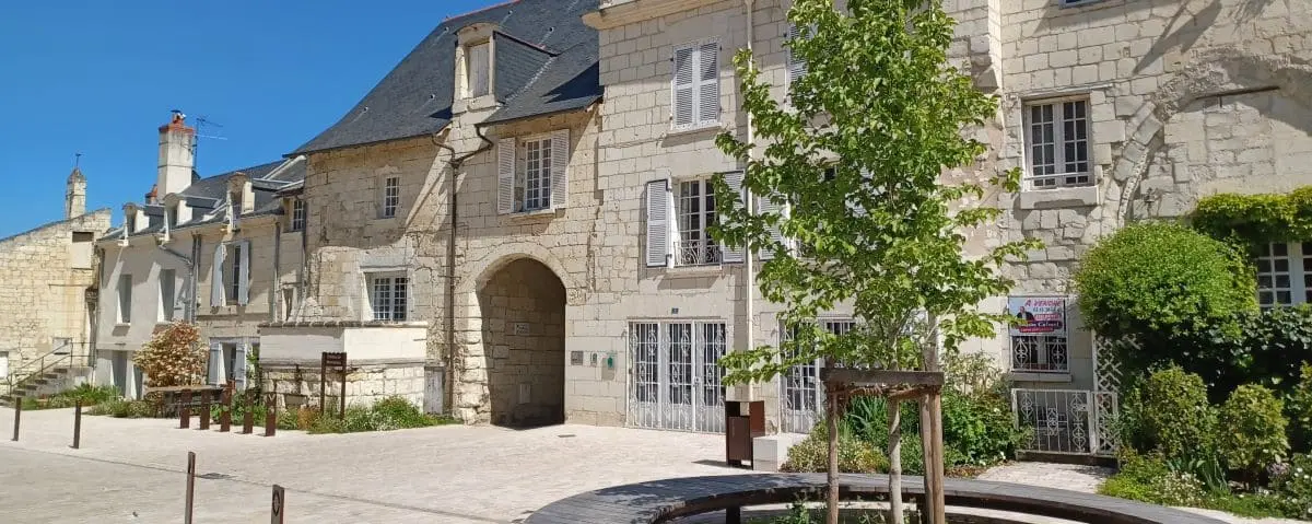 A charming street in Montsoreau lined with historic stone buildings and lush greenery, bathed in sunlight.