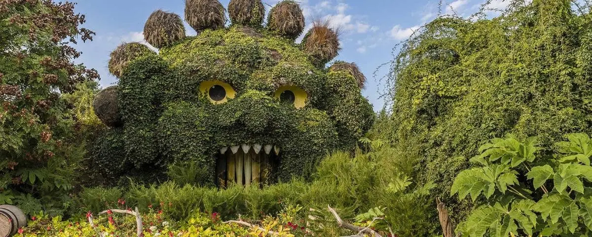 Entrance to Terra Botanica featuring a large green monster sculpture made of plants, with wide eyes and a mouth, surrounded by lush greenery.