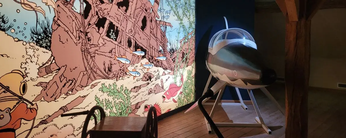 A display at the Tintin exhibition in Cheverny featuring a model of a submarine and a detailed mural of an underwater scene with fish and a sunken ship.