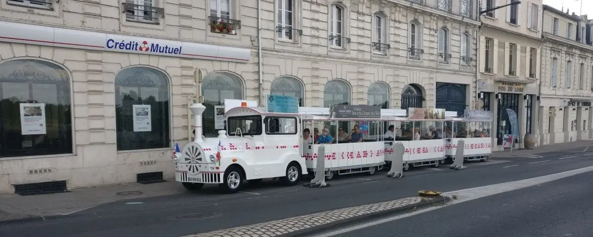 A white tourist train parked on the street in Saumur, with passengers seated inside, ready to explore the city's attractions.