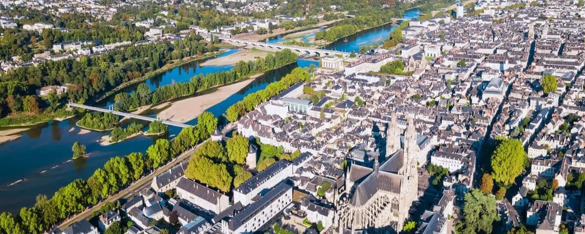 Panoramic aerial view of Tours town with the Loire River running through, showcasing historic buildings, bridges, and extensive green spaces.