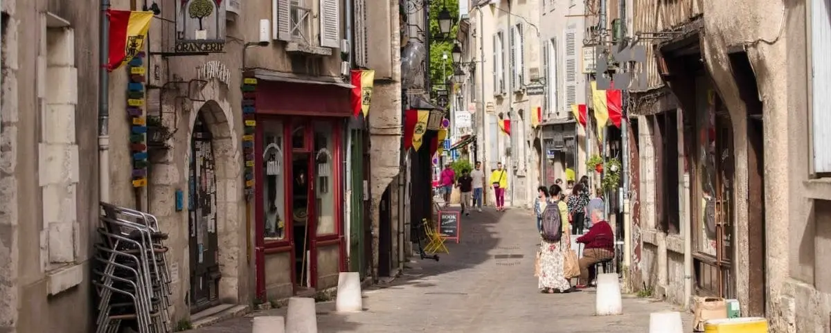A quaint town center with narrow streets lined with shops and decorated with flags, bustling with pedestrians.