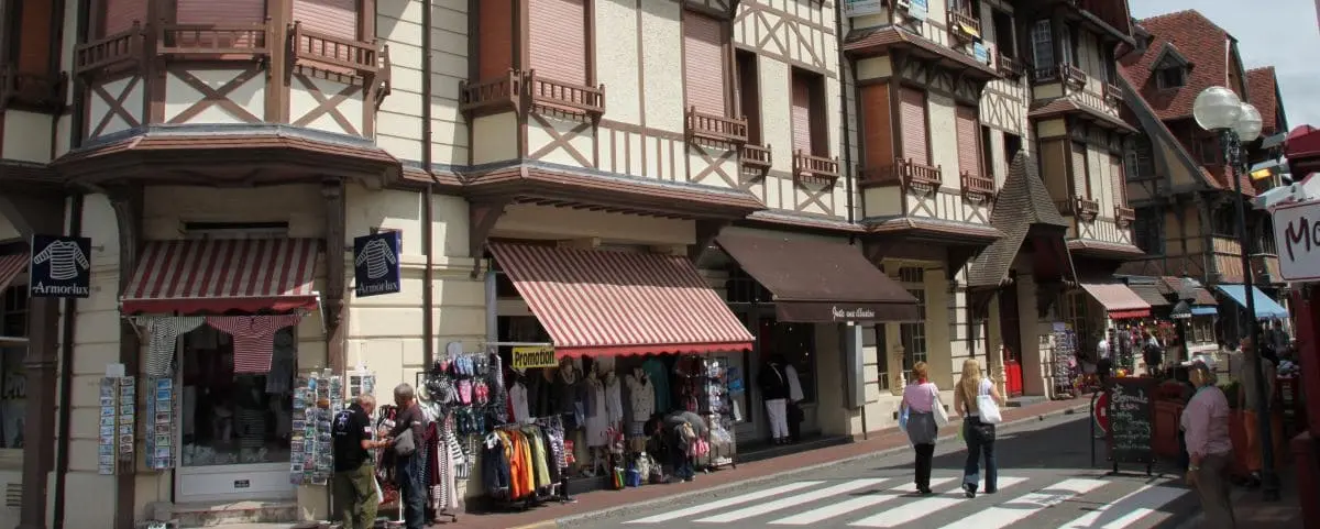 Bustling town center in Etretat, featuring half-timbered buildings, shops with striped awnings, and pedestrians crossing the street.