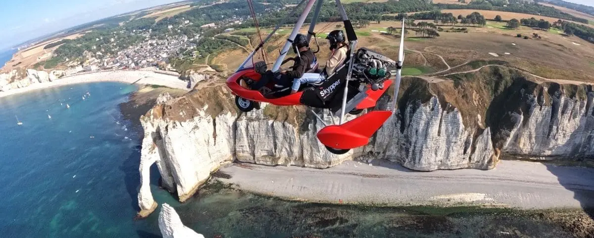 An ultralight aircraft flying over the stunning white cliffs and blue sea of Etretat, offering a bird's-eye view of the landscape.