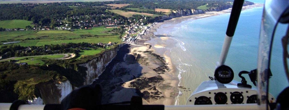 An aerial view from an ultralight trike flying over the cliffs and coastline of Dieppe, showing the beach, ocean, and green fields below.