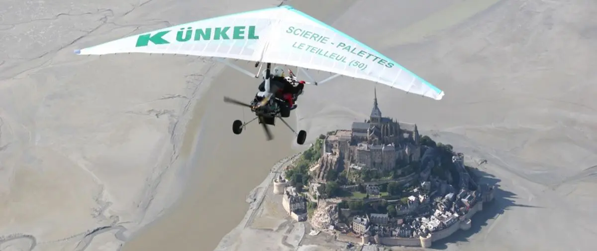 An ultralight trike flies over Mont Saint-Michel, offering a bird's-eye view of the island and its structures.