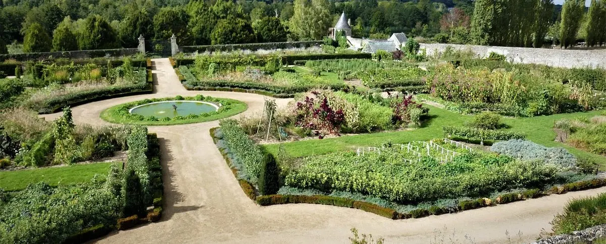 An expansive, well-kept garden with various plants, flowers, and a central circular pond, surrounded by green pathways and neatly trimmed hedges.