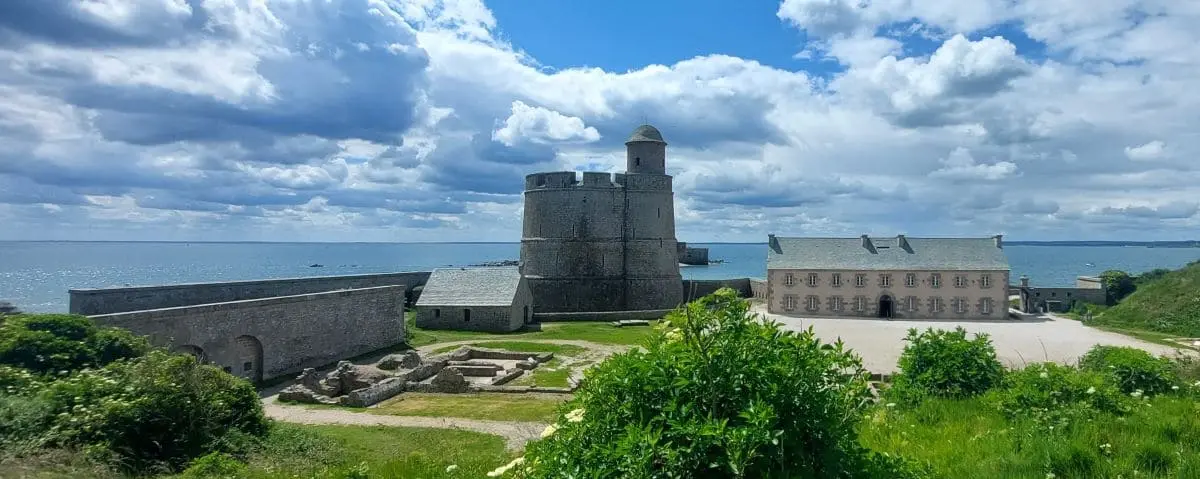 Vauban Tower on Tatihou Island, a historic fortification with surrounding ruins, set against a backdrop of the ocean.