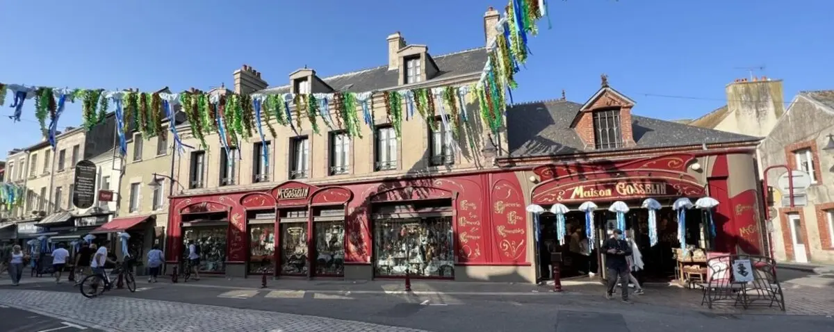 Verrue Street in Saint Vaast La Hougue, adorned with festive decorations, featuring historic buildings with vibrant storefronts.