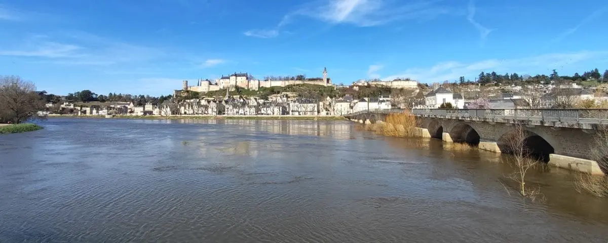 A panoramic view from a viewpoint overlooking Chinon Fortress, with the fortress and surrounding townscape reflected in the calm river below.