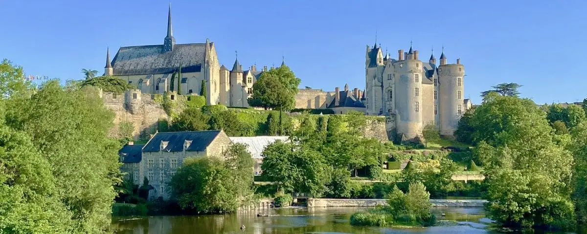 A scenic view from Napoleon Bridge in Montreuil-Bellay, overlooking a river, lush greenery, and the majestic castle in the background.