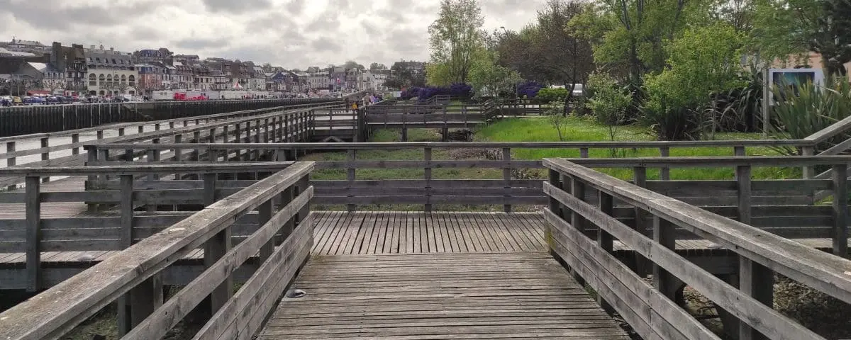 Wooden pathways along the Touques River in Deauville, with the town and green areas in the background.