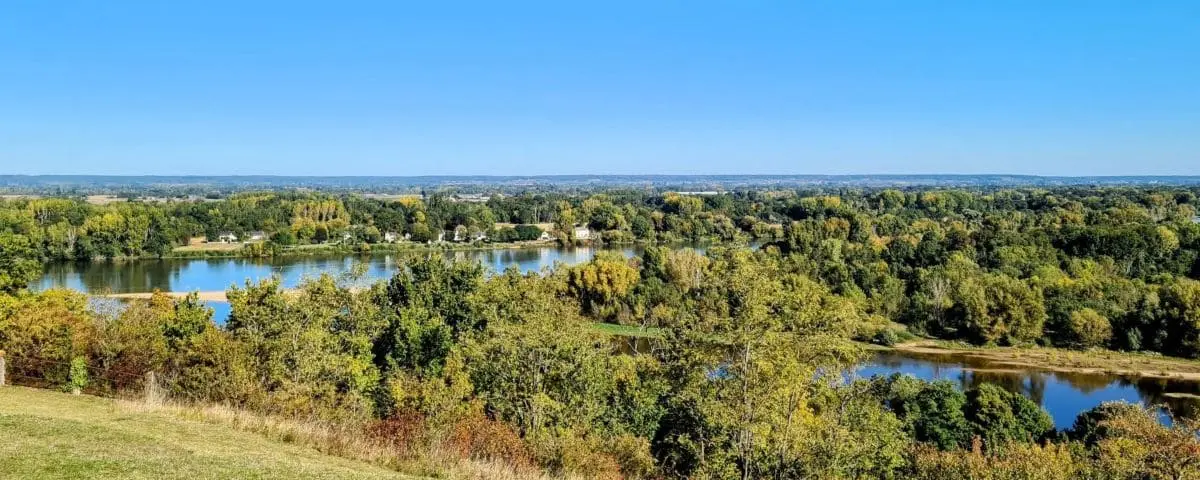 A panoramic view of Candes-Saint-Martin, showcasing the village nestled amidst lush greenery and a winding river, under a bright blue sky.