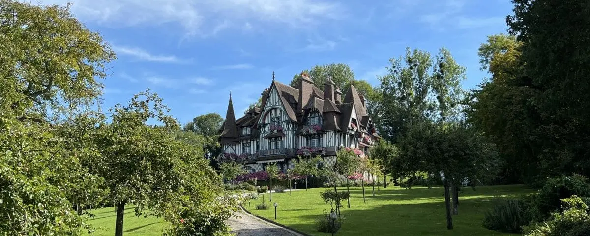 The historic Villa Strassburger in Deauville, surrounded by lush greenery and gardens on a sunny day.
