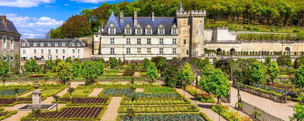 View of Villandry Castle with its meticulously maintained Renaissance gardens featuring symmetrical patterns of hedges, plants, and colorful flowers.
