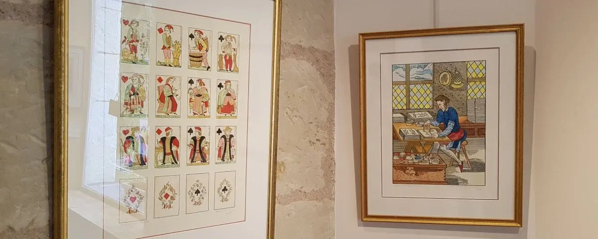 A display of framed artworks at the Festina Lente workshop in Fontevraud-Bellay, featuring detailed illustrations and colorful designs.